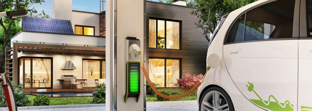 Charging an electric car in the garage near the house. Modern house with solar panels on the roof.