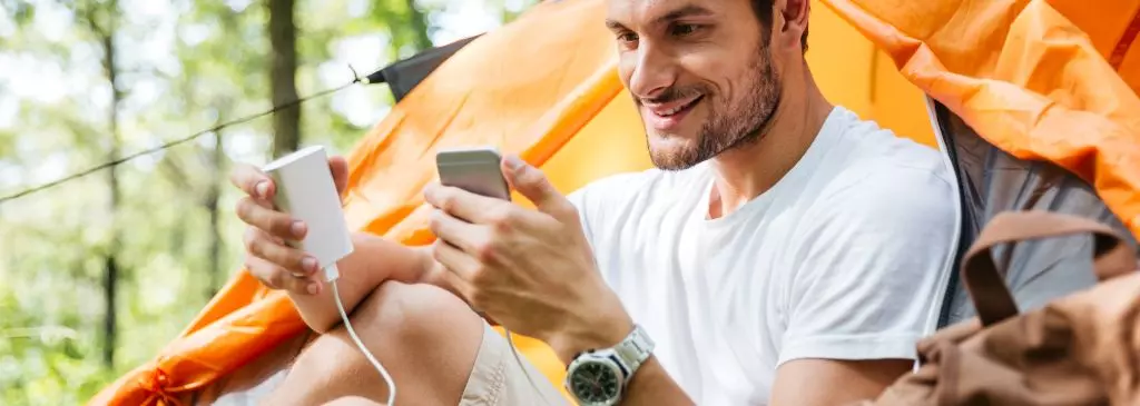 Man tourist charging battery of mobile phone in touristic tent