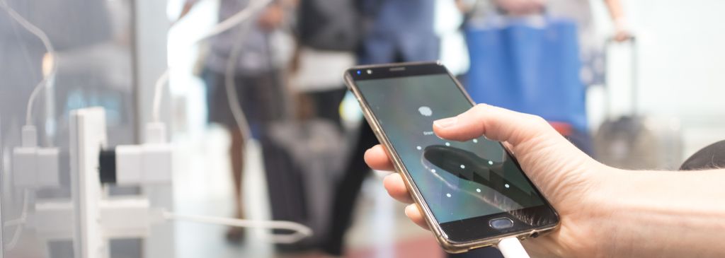 Female hands holding and using smartphone while charging it in a public place using electric plug and a charging cable