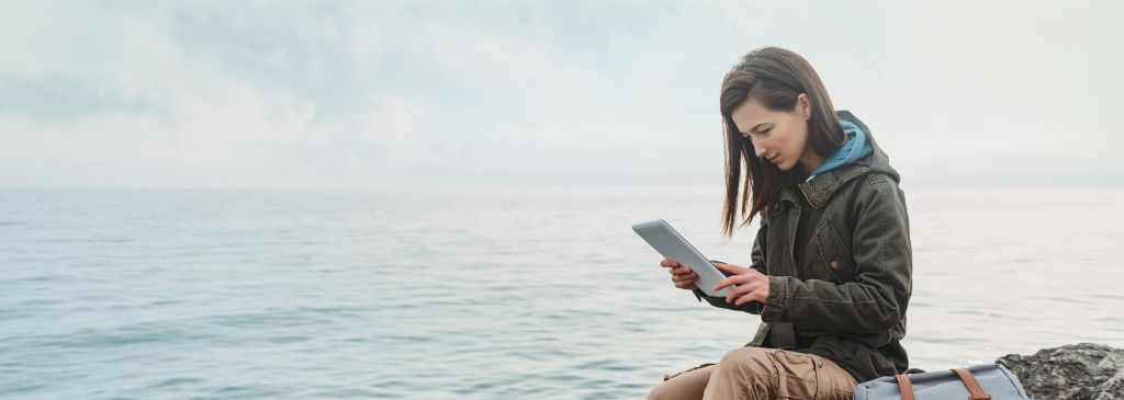 Traveler woman sitting on coast with digital tablet